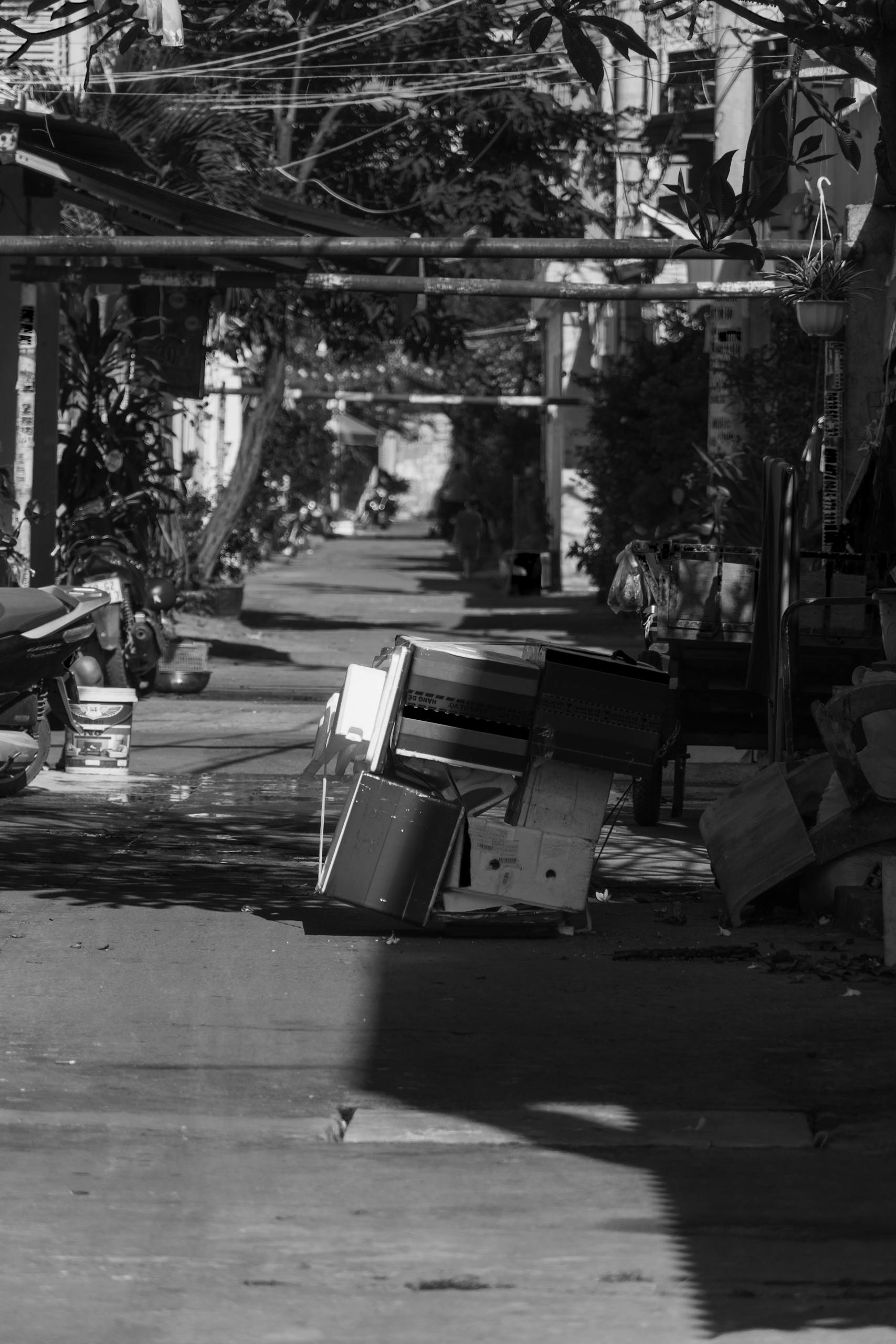 A black and white photo of an urban alleyway cluttered with discarded furniture, creating a sense of mystery.